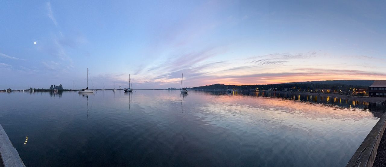 Sailboats moored in Grand Marais harbor at sunset, with the town lights reflecting on the water